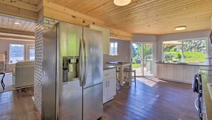 A modern kitchen with a stainless steel refrigerator, wooden ceiling, and large windows offering a view of the outdoors. - Waterfront Gig Harbor Home w/ Furnished Deck (Gig Harbor)