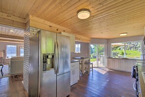 A modern kitchen with a stainless steel refrigerator, wooden ceiling, and large windows offering a view of the outdoors. - Waterfront Gig Harbor Home w/ Furnished Deck (Gig Harbor)