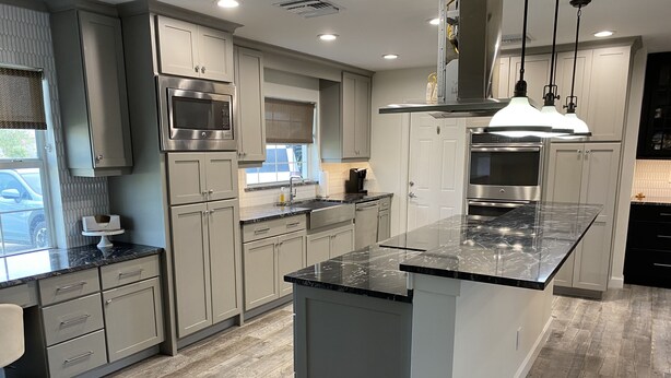 A modern kitchen with grey cabinets, stainless steel appliances, and a marble countertop.