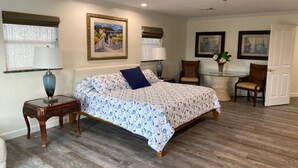 A bedroom with a bed, a side table, a chair, a small table with a plant, and a door.
