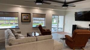A modern living room with a sectional sofa, a brown armchair, a flat-screen TV, and ceiling fans.