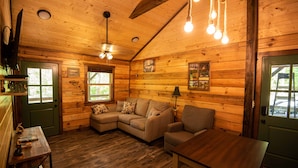 A cozy cabin interior with a wooden interior, a sectional sofa, a small table, and a ceiling fan. - The Gilead Log Cabin (Harriet)
