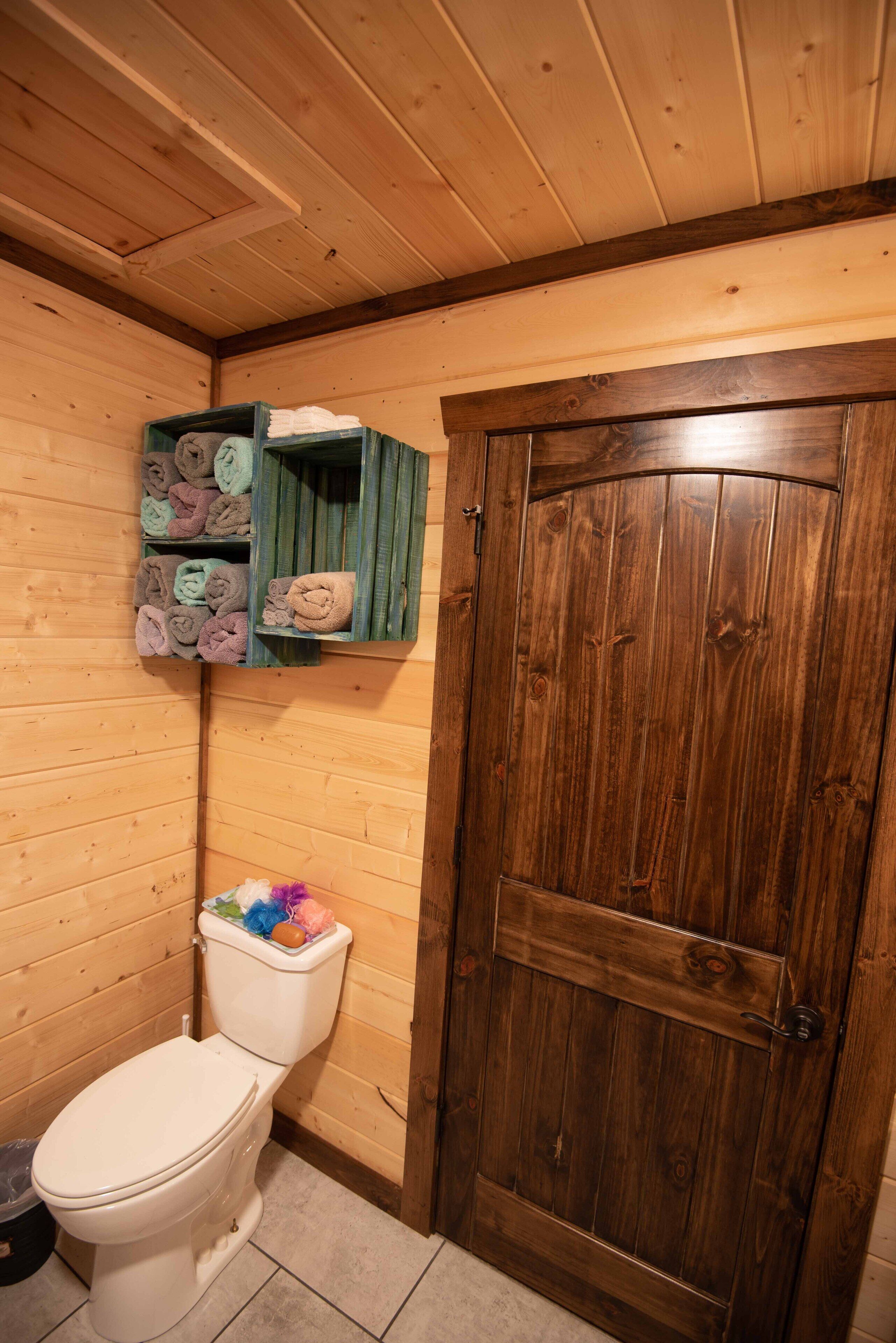 Un baño de madera con inodoro, una puerta de madera y un estante con toallas.