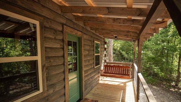 A wooden cabin with a porch, a green door, and a bench. - The Gilead Log Cabin (Harriet)