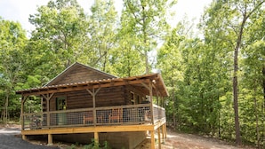 A wooden cabin with a porch and a fenced-in area, surrounded by trees. - The Gilead Log Cabin (Harriet)