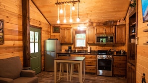 A wooden cabin interior with a kitchen, dining area, and a green door. - The Gilead Log Cabin (Harriet)