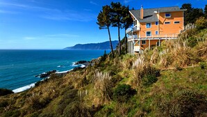 Una casa costera con balcón que da al mar, rodeada de vegetación natural.