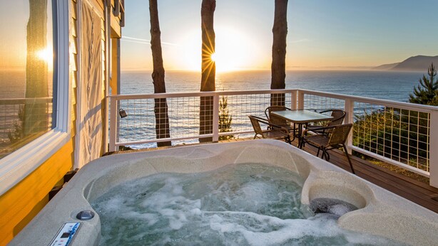 Un jacuzzi en una terraza con vistas al océano y al atardecer.