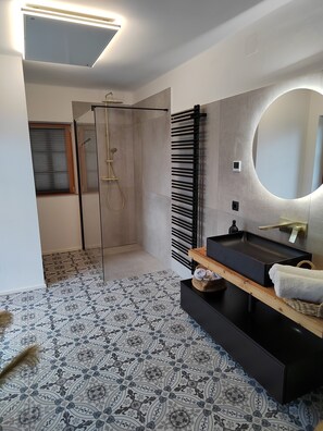 Un baño moderno con cabina de ducha de vidrio, un lavamanos negro sobre encimera de madera y baldosas de suelo estampadas.