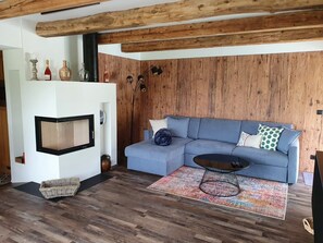 A living room with a blue sofa, a black coffee table, a patterned rug, wooden flooring, and a wooden wall panel.