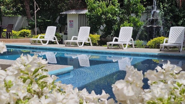 A pool area with white lounge chairs and a small building in the background. - Rancho la Esmeralda  (Playa Sandiego)