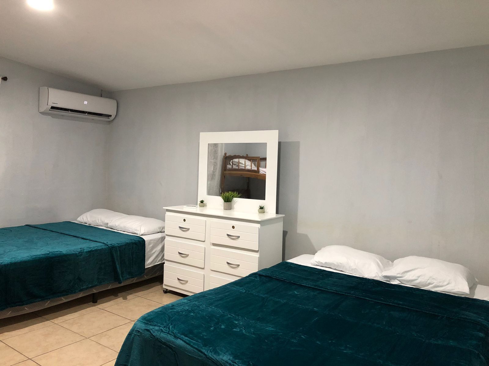 A bedroom with two beds, a dresser, a mirror, and an air conditioning unit.
