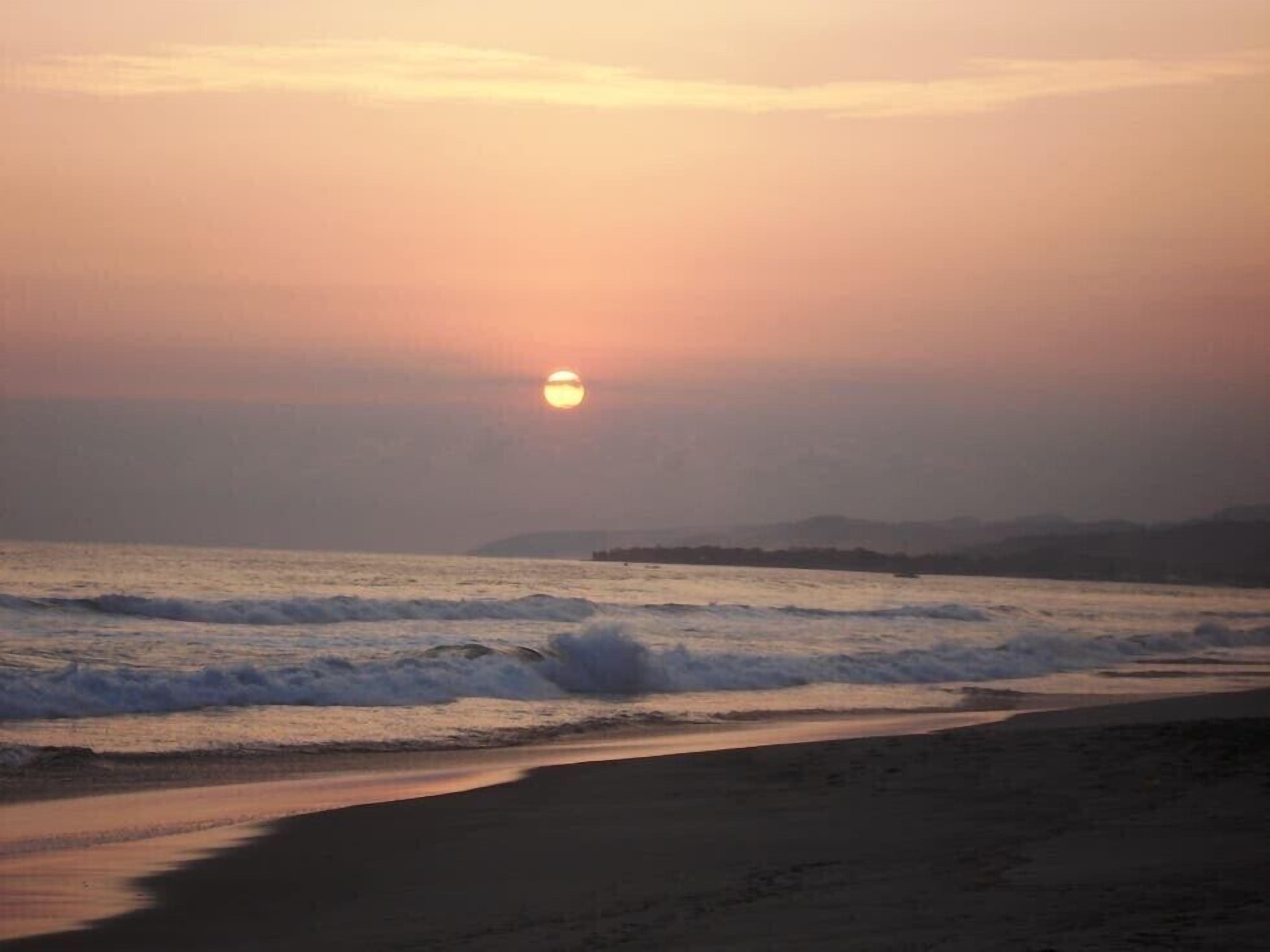 Platja amb onades i un cel ocre al fons.