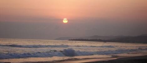 Platja amb onades i un cel ocre al fons.