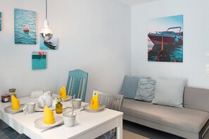 A dining area with a table set for two, a sofa, and wall art depicting boats.