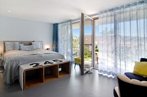 A modern bedroom with a bed, a bench with numbers, a chair, and a view through a glass door.