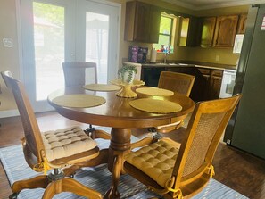 Un comedor con una mesa redonda de madera, seis sillas con asientos de mimbre y un elemento decorativo en el centro.