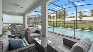 Un patio al aire libre con mobiliario de mimbre, un ventilador de techo y vista a una piscina.