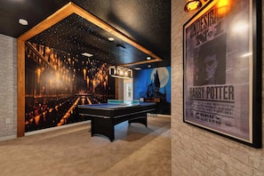 Una mesa de billar en una habitación con un mural de un mago y un cartel de Harry Potter número 1.