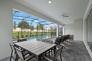 Un patio cubierto con vista a la piscina, mobiliario exterior y un ventilador de techo.