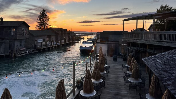 Ein Restaurant am Wasser mit Außenbereich, das auf einen Fluss blickt, mit Holzhäusern und einem Boot im Hintergrund.