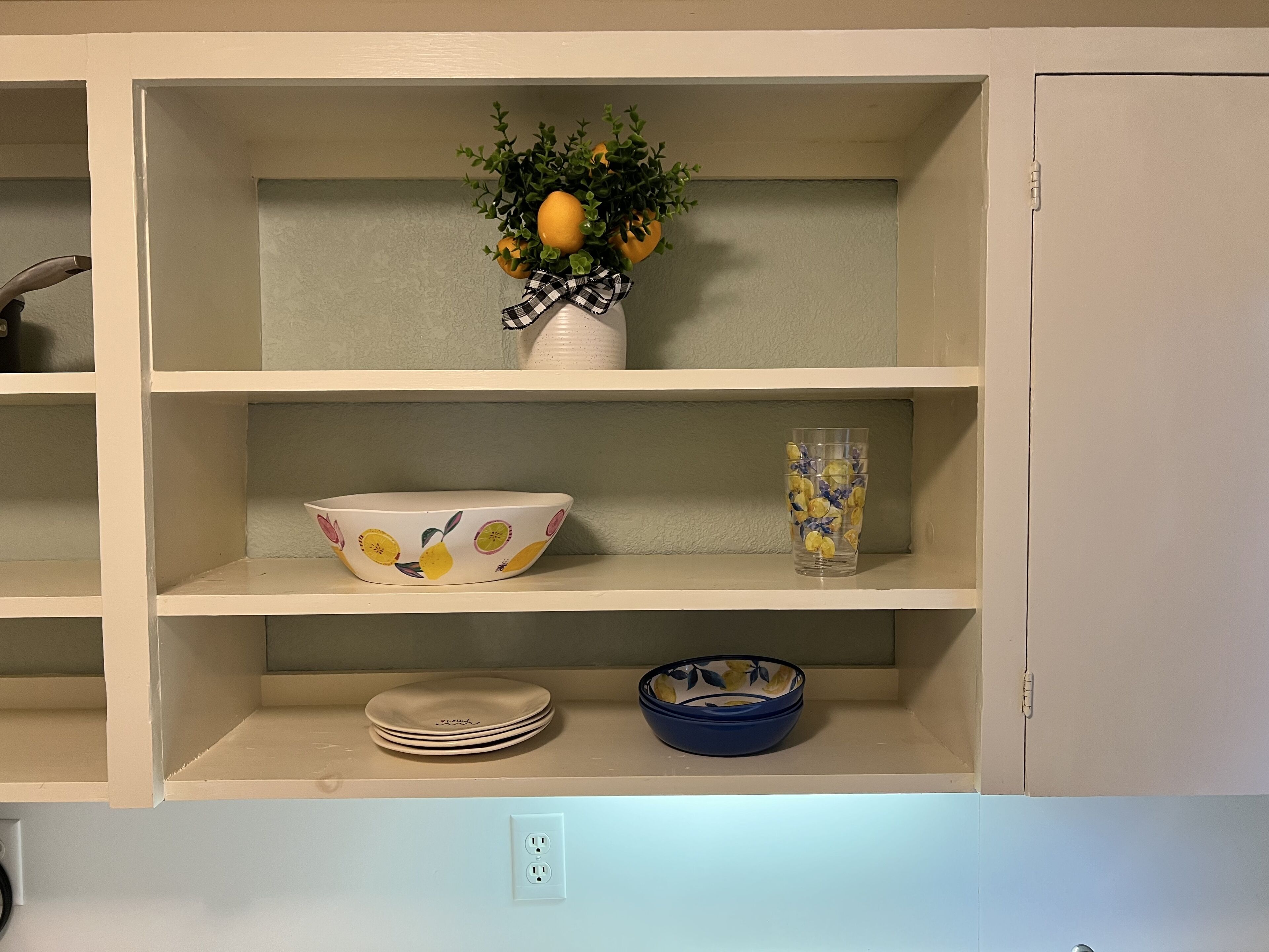 A kitchen shelf with a bowl, a glass, and a potted plant.
