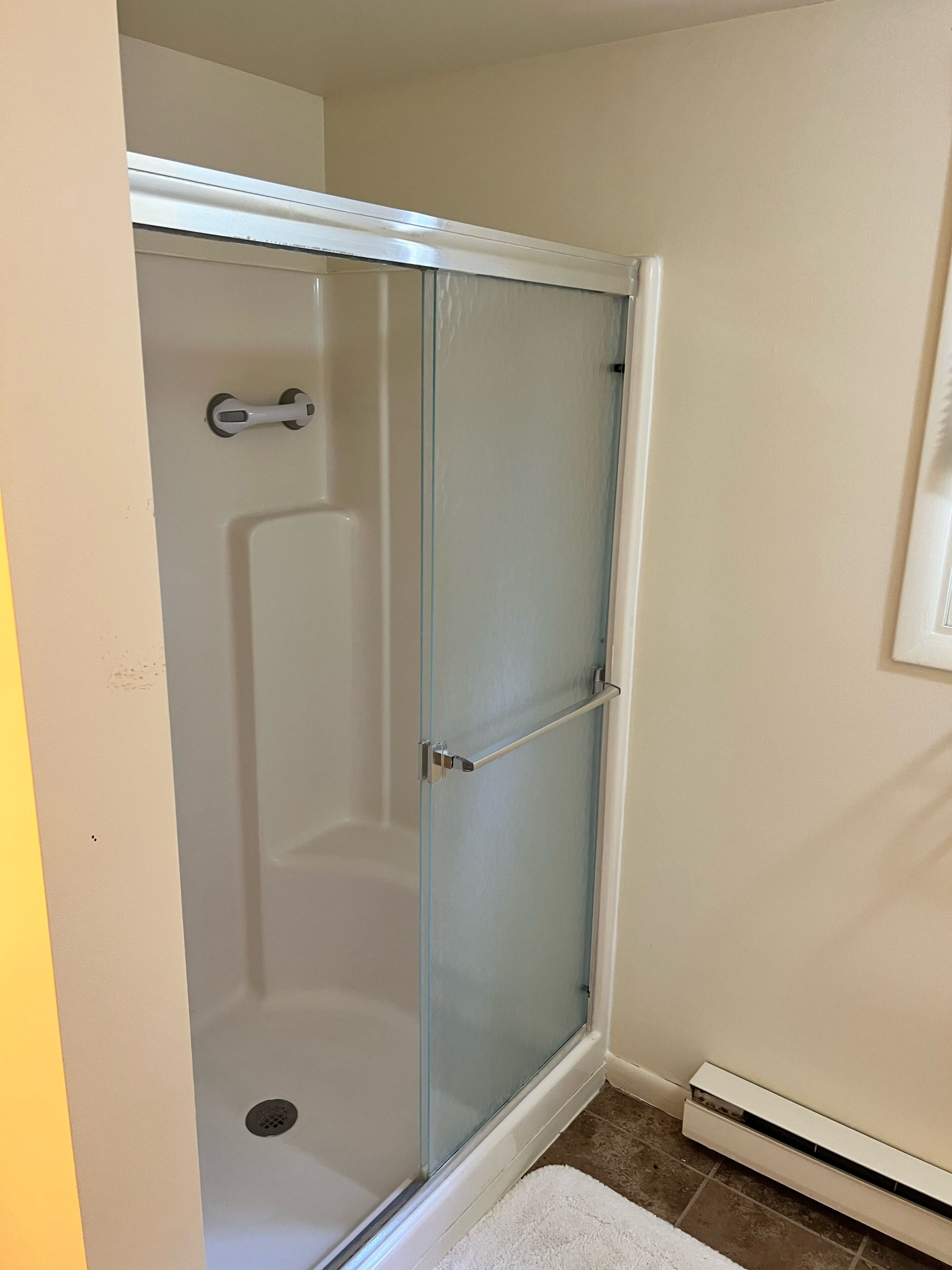 A shower with a glass door, a towel rack, and a vent on the wall.