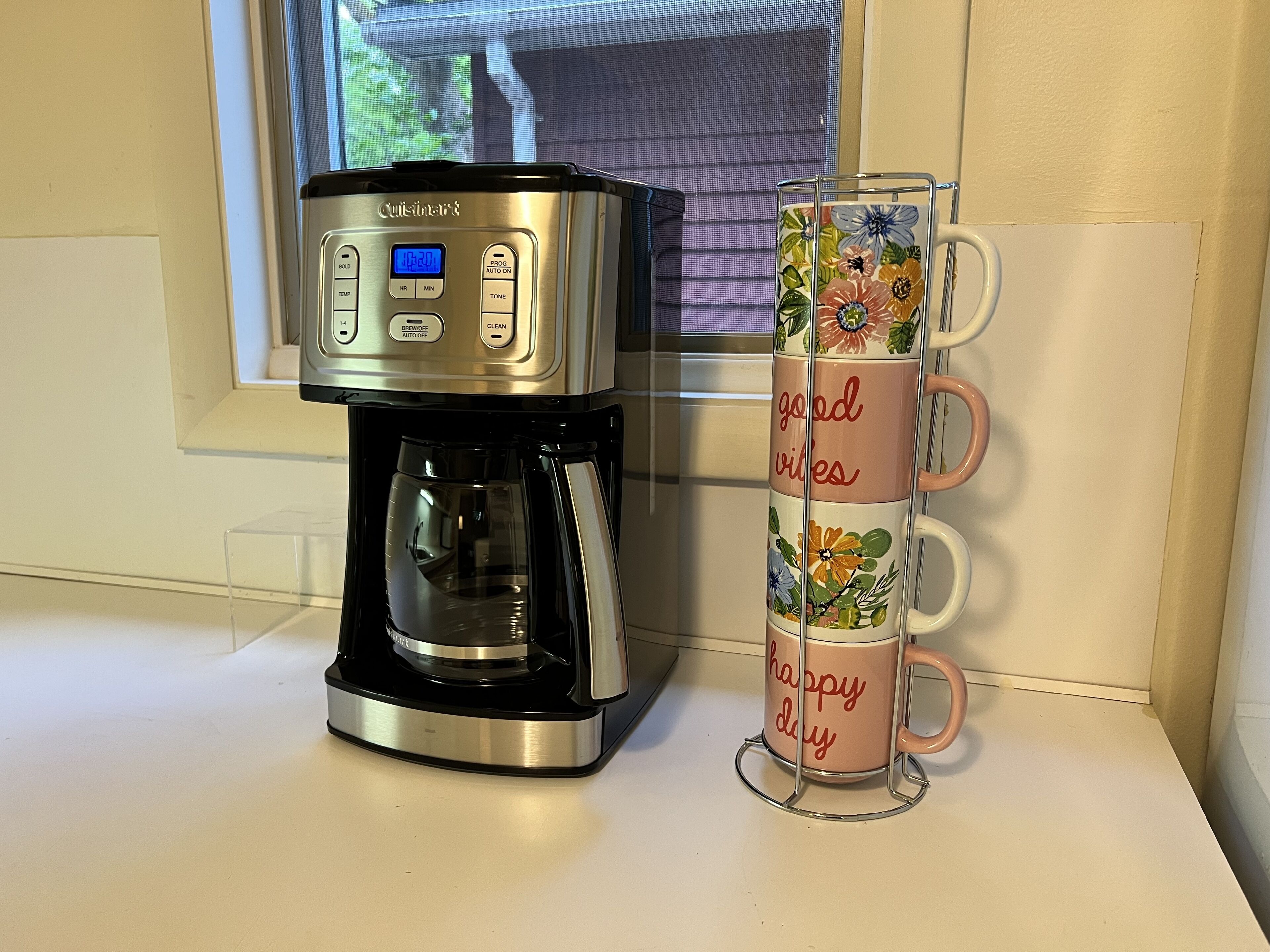 Eine Kaffeemaschine mit digitalem Display und Stapel Tassen mit den Aufschriften 'good vibes' und 'happy day'.