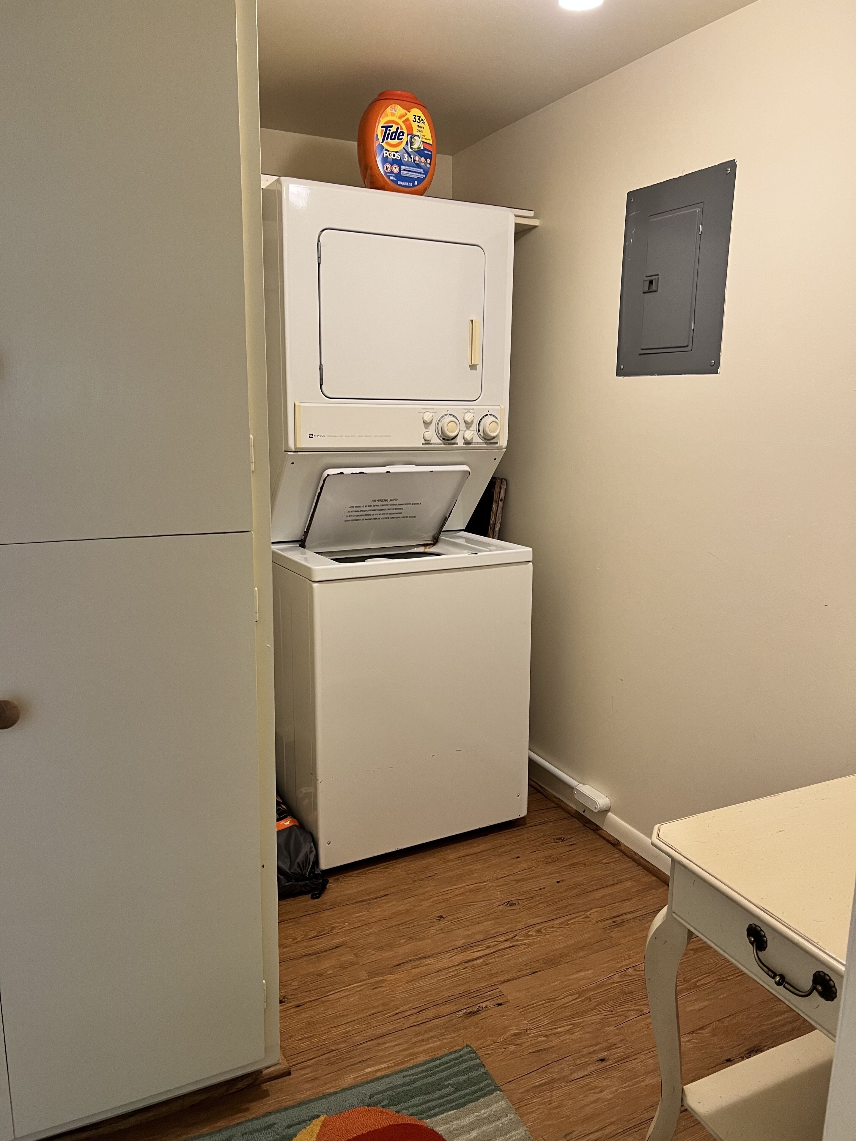A compact laundry room with a front-loading washer and dryer, a small table, and a door.