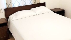 Ein ordentlich bezogenes Bett mit weißen Leinentüchern, einem Holzkopfteil und einem Nachttisch mit Lampe.