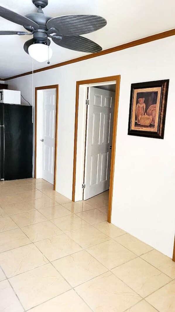 A hallway with a ceiling fan, two white doors, a framed picture on the wall, and a tiled floor.