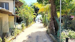 Eine schmale, unbefestigte Straße, gesäumt von Wohnhäusern und üppigem Grün.