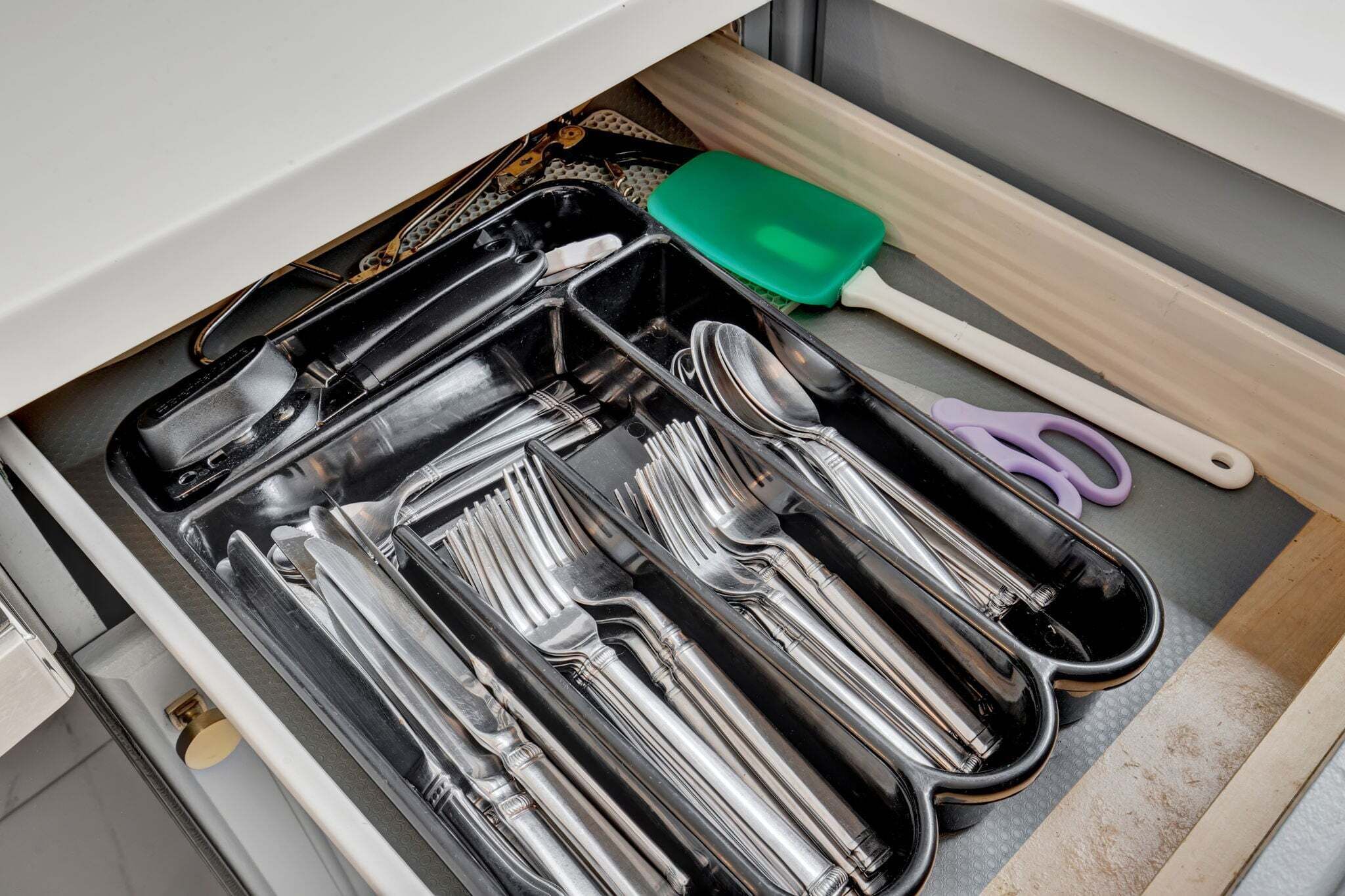 Un cassetto con utensili da cucina e una spatola verde.