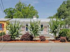 A two-story house with a porch, a chimney, and a small garden with shrubs and trees.