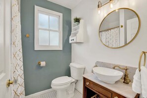 A bathroom with a toilet, sink, mirror, and a window.