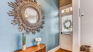 Una habitación con pared azul, un espejo decorativo, una consola de madera con jarrones y una puerta con un letrero.