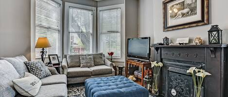 A living room with a sofa, ottoman, fireplace, television, and framed artwork.