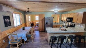 A cabin-style kitchen with wooden cabinets, a refrigerator, a microwave, and a dining area with a table and chairs.