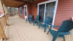 A covered porch with wooden railings, a set of four green Adirondack chairs, and a sliding glass door.