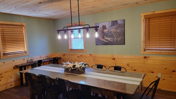 A dining area with a wooden table, chairs, a chandelier, and a painting on the wall.
