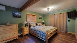 A bedroom with a wooden bed, two bedside tables with lamps, a dresser, a window with blinds, and a ceiling fan.