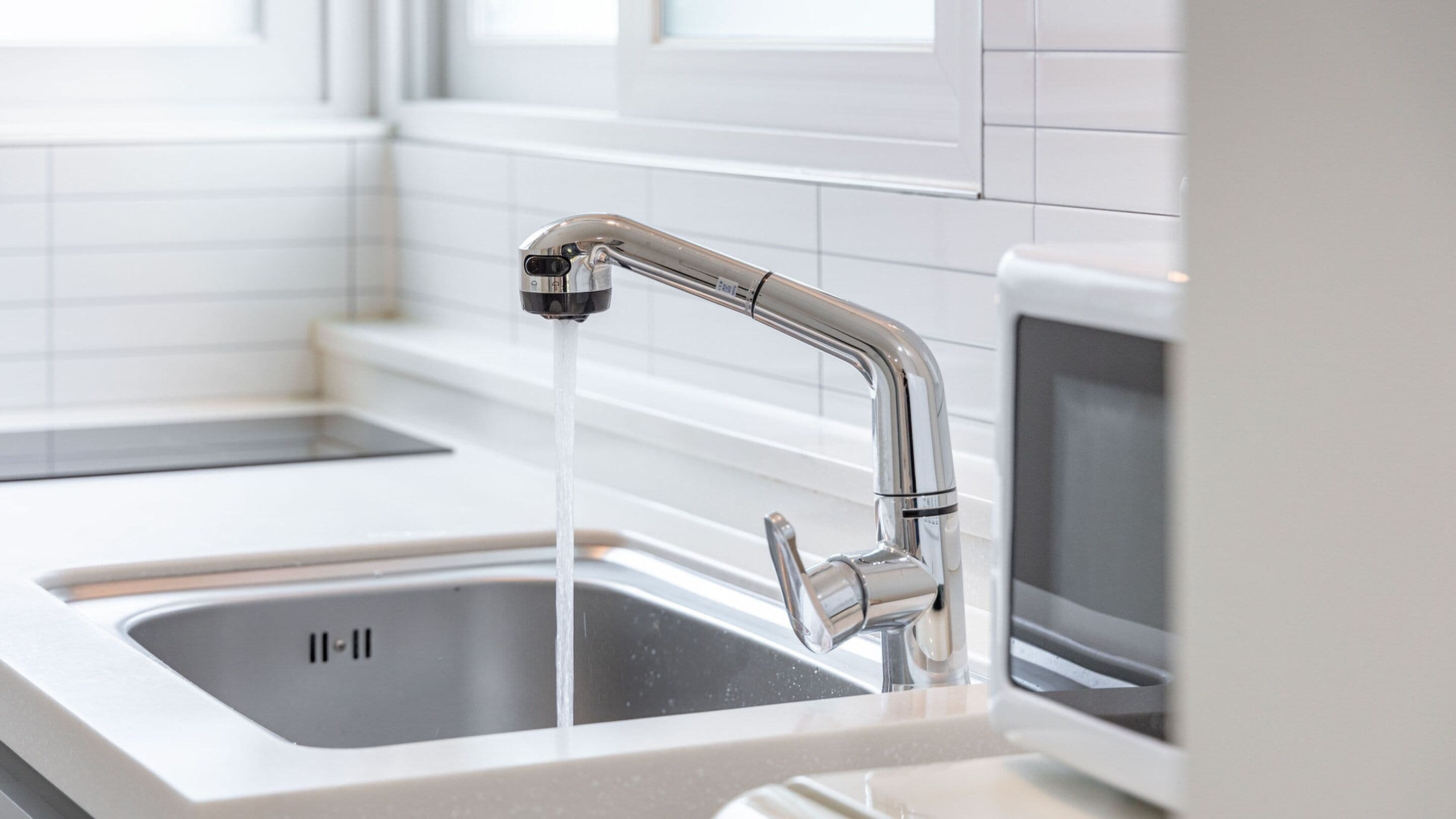 A modern kitchen with a stainless steel faucet, a double sink, and white tiled walls.