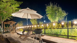 An outdoor patio area with a wooden table and a barbecue grill, surrounded by a wooden fence and string lights. - Hongcheon Toliaigeullaemping (Hongcheon)