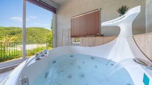 A modern bathroom with a large bathtub, a wooden bench, and a view of a green landscape. - Hongcheon Toliaigeullaemping (Hongcheon)