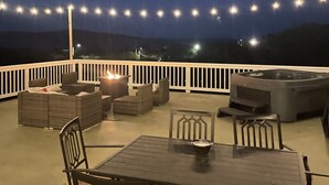 En udendørs terrasse med et bord, stole, pejse og lyskæder.