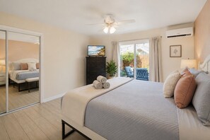 A bedroom with a bed, a ceiling fan, a TV, a sliding glass door, and a view of the outdoors.
