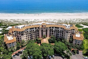Un hotel grande de varios pisos con techo curvo, rodeado de abundante vegetación y vistas a la playa.