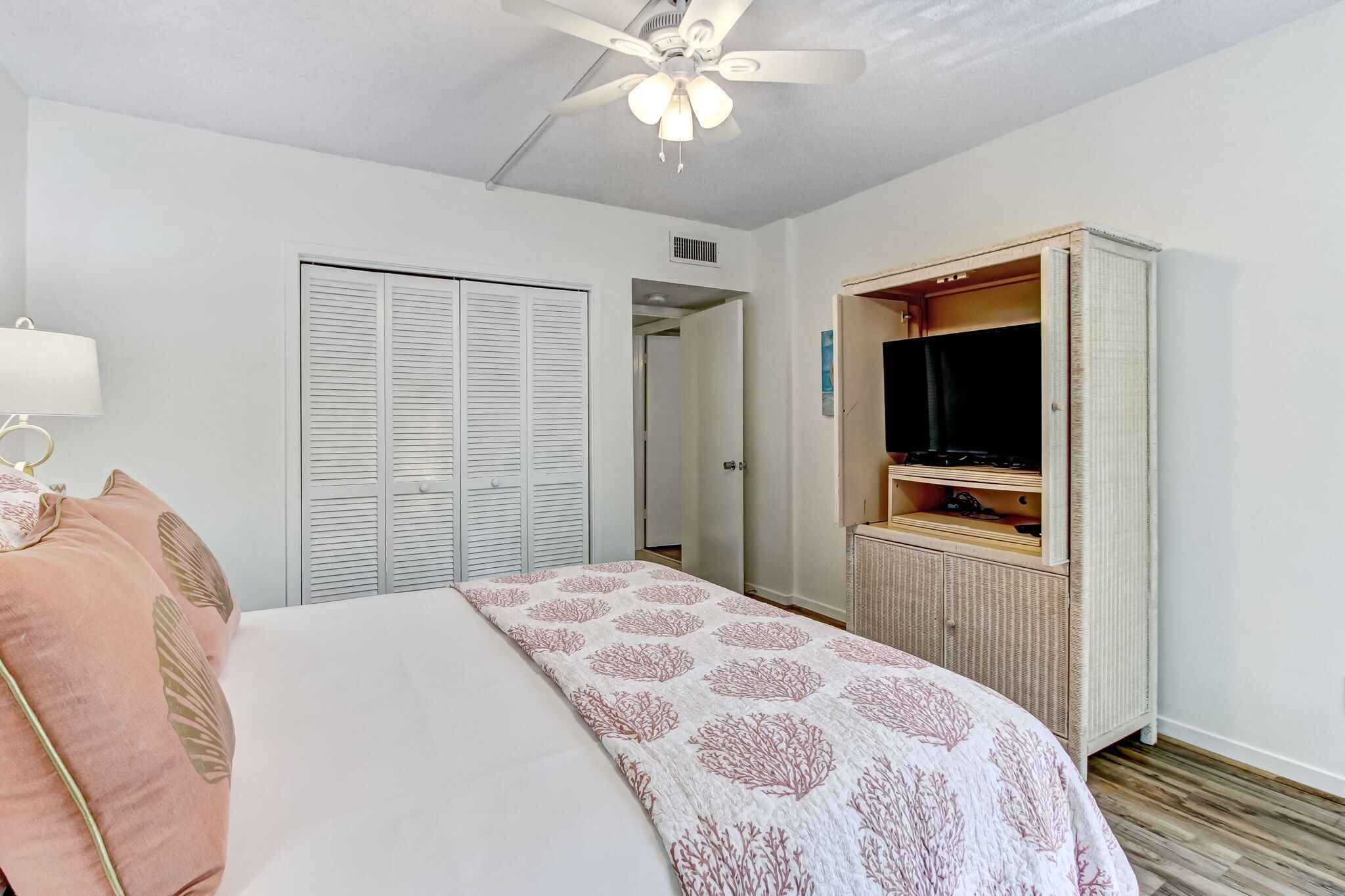 Une chambre à coucher comprenant un lit, un ventilateur de plafond, une armoire et un téléviseur.
