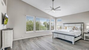Quarto com uma cama grande, um ventilador de teto e várias janelas com persianas.
