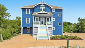 Een blauw huis met twee verdiepingen, een veranda en een kleurrijke trap.